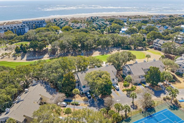 Un quartier résidentiel situé sur la côte, avec des maisons, un terrain de golf et une plage en arrière-plan.