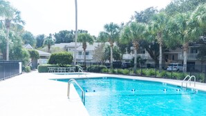 A swimming pool with a metal ladder, surrounded by a fence and palm trees. - Fairway Dunes 27 - Screen Porch Golf Course View! (Isle of Palms)