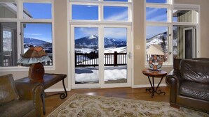 A room with large windows, a brown leather sofa, a patterned rug, and a small table with a lamp. - Silver Lane (Mt. Crested Butte)