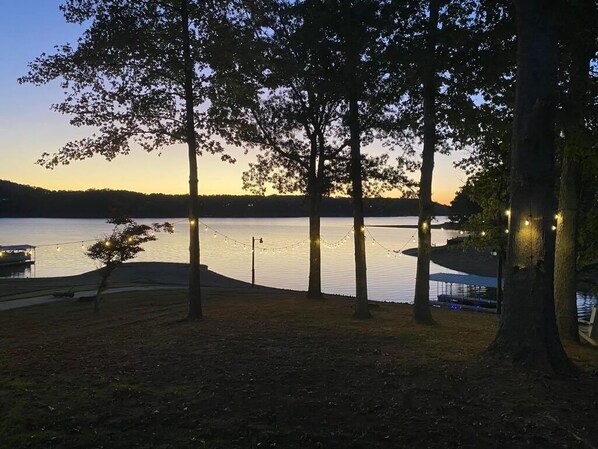 A lakeside park at dusk with trees and string lights.