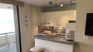 Une cuisine moderne dotée d’un îlot central, de deux tabourets de bar, d’une machine à café et offrant une vue sur l’océan grâce à une porte coulissante.