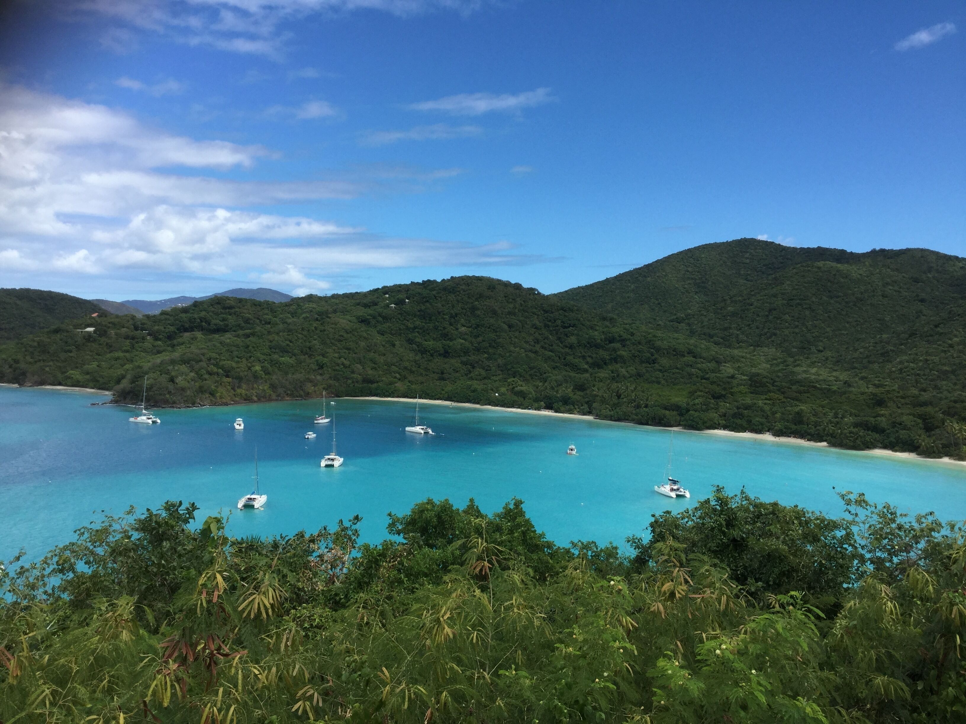 A coastal landscape with clear turquoise waters, boats, and lush green hills.