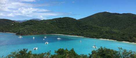 A coastal landscape with clear turquoise waters, boats, and lush green hills.