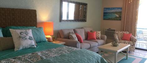 A well-lit room with a bed, two sofas, a coffee table, and a painting on the wall.