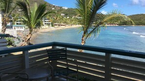 Un balcon avec vue sur une plage, des palmiers et des bâtiments en arrière-plan.