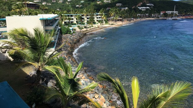 Un hôtel situé sur la côte, offrant une vue sur la plage, bordé d’une côte rocheuse et ayant des collines en arrière-plan.