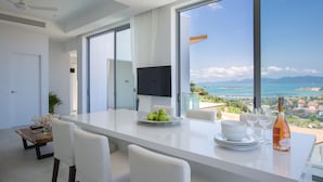 Un espace de restauration moderne avec une grande table, des chaises blanches et une vue imprenable sur l’océan.