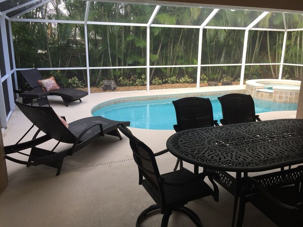 A covered outdoor area with a pool, lounge chairs, and a table.