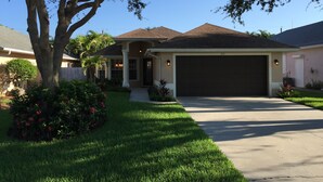 A residential house with a large garage, a well-maintained lawn, and mature trees. - 5⭐️ LUXURY BEACH VILLA with SECLUDED HEATED POOL+HOT TUB SURROUNDED by PALM TREES (Naples)