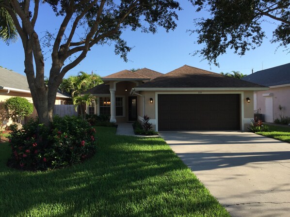 A residential house with a large garage, a well-maintained lawn, and mature trees. - 5⭐️ LUXURY BEACH VILLA with SECLUDED HEATED POOL+HOT TUB SURROUNDED by PALM TREES (Naples)