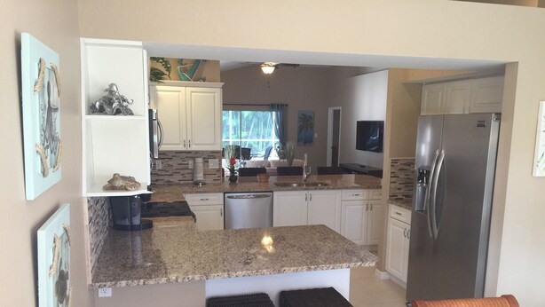 A modern kitchen with granite countertops, white cabinetry, a built-in dishwasher, and a stainless steel refrigerator. - 5⭐️ LUXURY BEACH VILLA with SECLUDED HEATED POOL+HOT TUB SURROUNDED by PALM TREES (Naples)