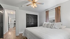 A bedroom with a large bed, a ceiling fan, and a door leading to a kitchen. - Walk-to-Lambeau Tailgate House (Green Bay)
