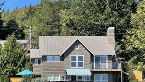 A two-story house with a dock extending into a body of water, surrounded by trees.