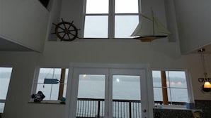 A room with a view of the sea, a sailboat decoration, and a ship's wheel.