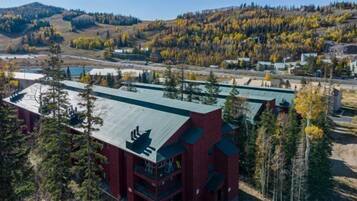 A multi-story building with a green roof, surrounded by trees and a hilly landscape.