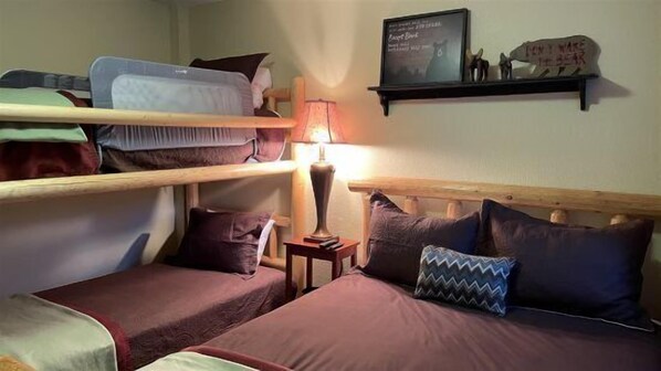 A dormitory room with bunk beds, a bedside table with a lamp, and a wall-mounted shelf with decorative items.