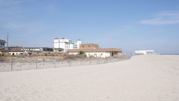 A beach with a fence, buildings, and a clear sky. - Stay in the Heart of Cape May at the Charming Rose Suite (Cape May)