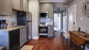 A modern kitchen with stainless steel appliances, a dishwasher, and a wooden dining table. - Stay in the Heart of Cape May at the Charming Rose Suite (Cape May)