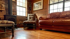 A cozy room with a wooden floor, a brown leather sofa, a patterned armchair, and a vintage fireplace. - Romantic Rock Cabin, Beautiful, Spectacular Views of Frio River & Mountains! (Concan)