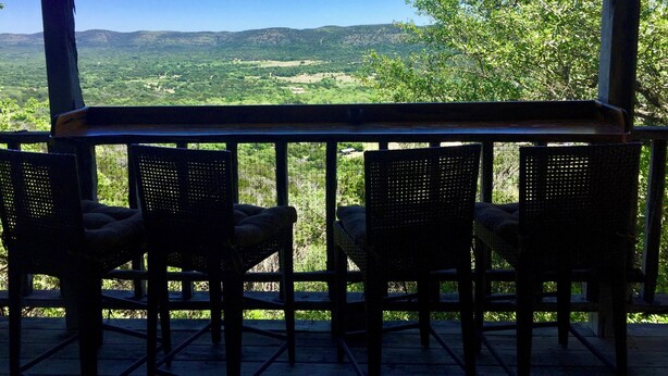 A terrace with wicker chairs and a table overlooking a mountainous landscape. - Romantic Rock Cabin, Beautiful, Spectacular Views of Frio River & Mountains! (Concan)