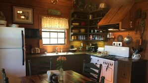 A cozy kitchen with wooden cabinets, a stove, and a dining table with chairs. - Romantic Rock Cabin, Beautiful, Spectacular Views of Frio River & Mountains! (Concan)