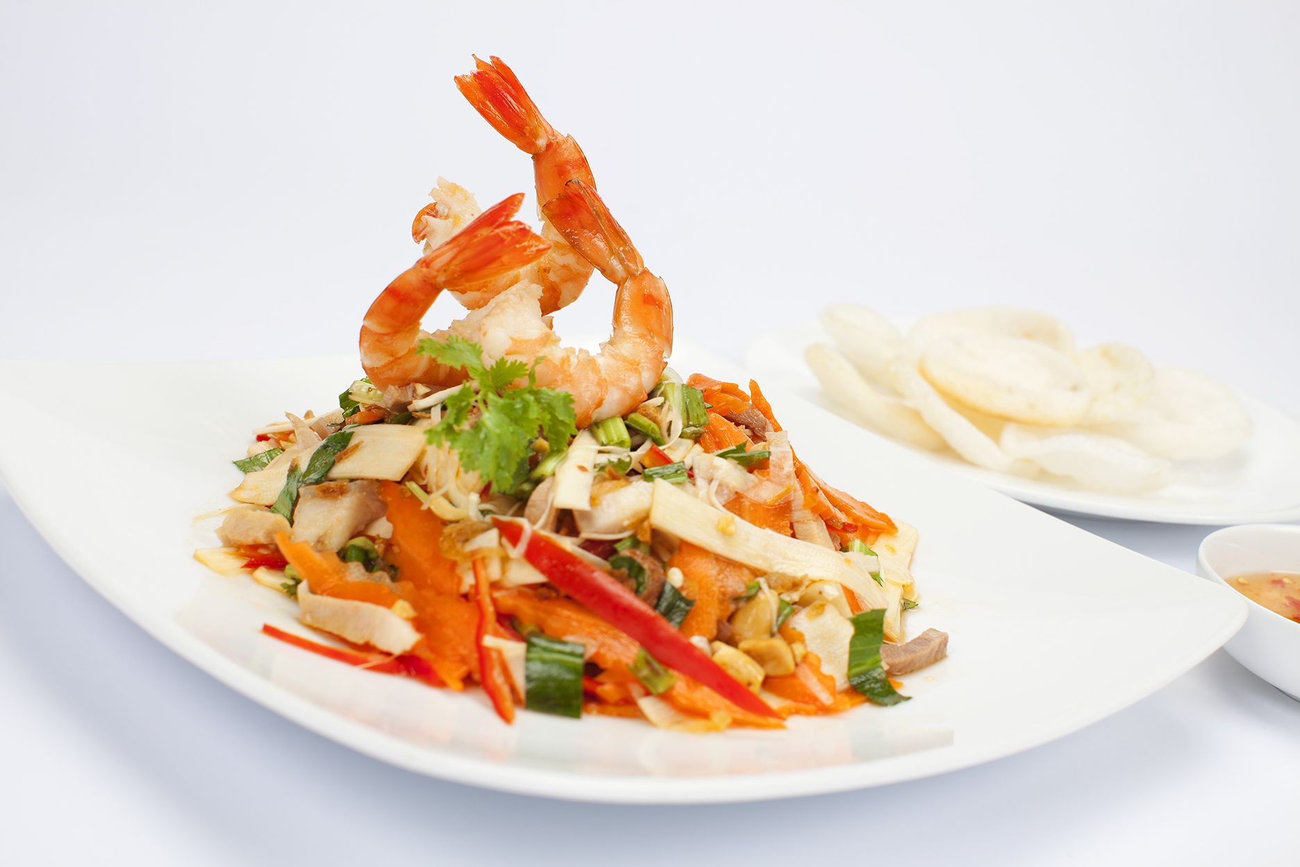 A plate of food with shrimp, vegetables, and noodles, accompanied by a bowl of soup and a plate of crackers.