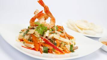A plate of food with shrimp, vegetables, and noodles, accompanied by a bowl of soup and a plate of crackers.