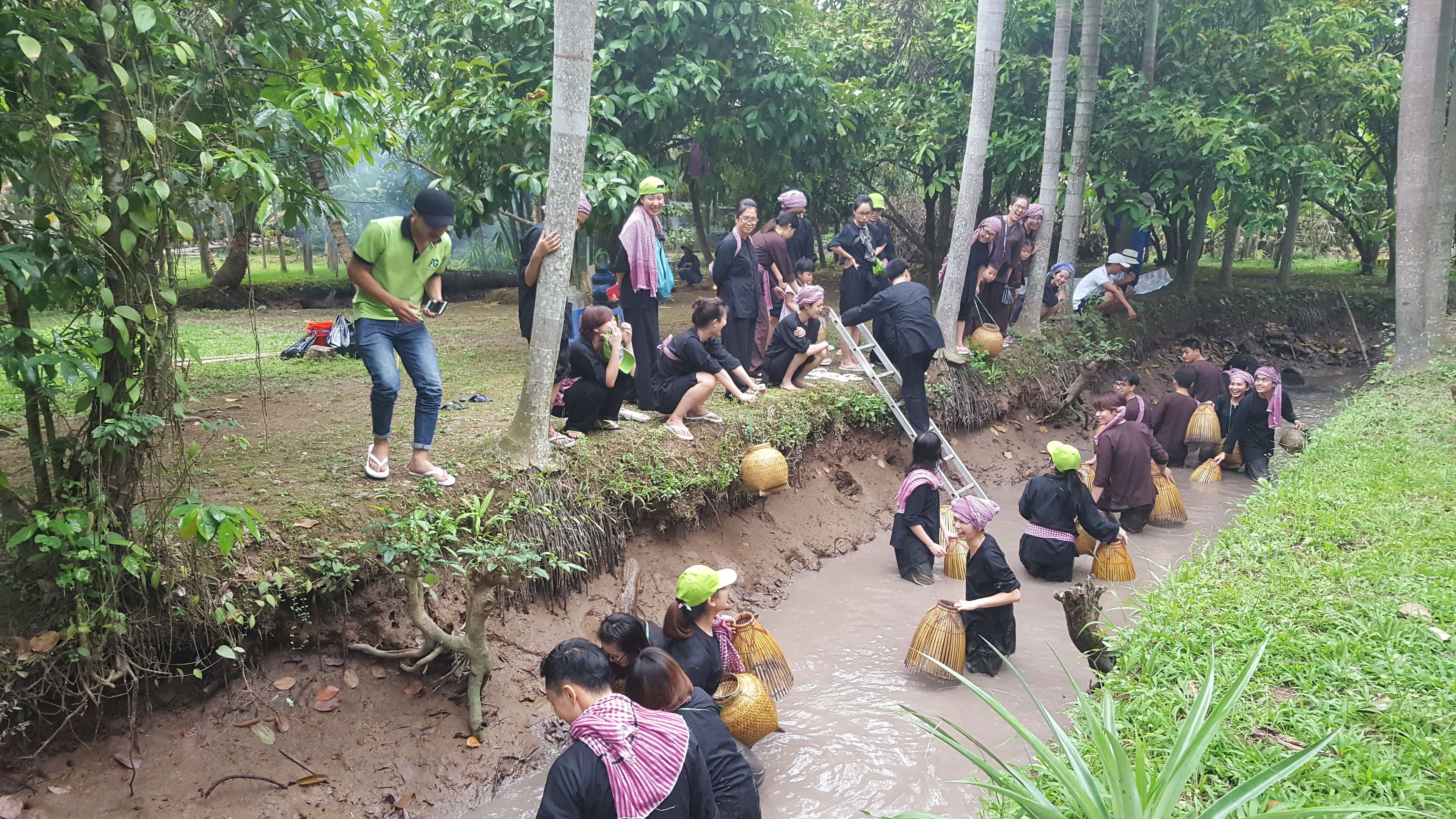 A group of people engaged in an outdoor activity near a water body, surrounded by greenery.