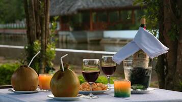 A table set with drinks, snacks, and a bottle of champagne, with a view of a thatched-roof building in the background.