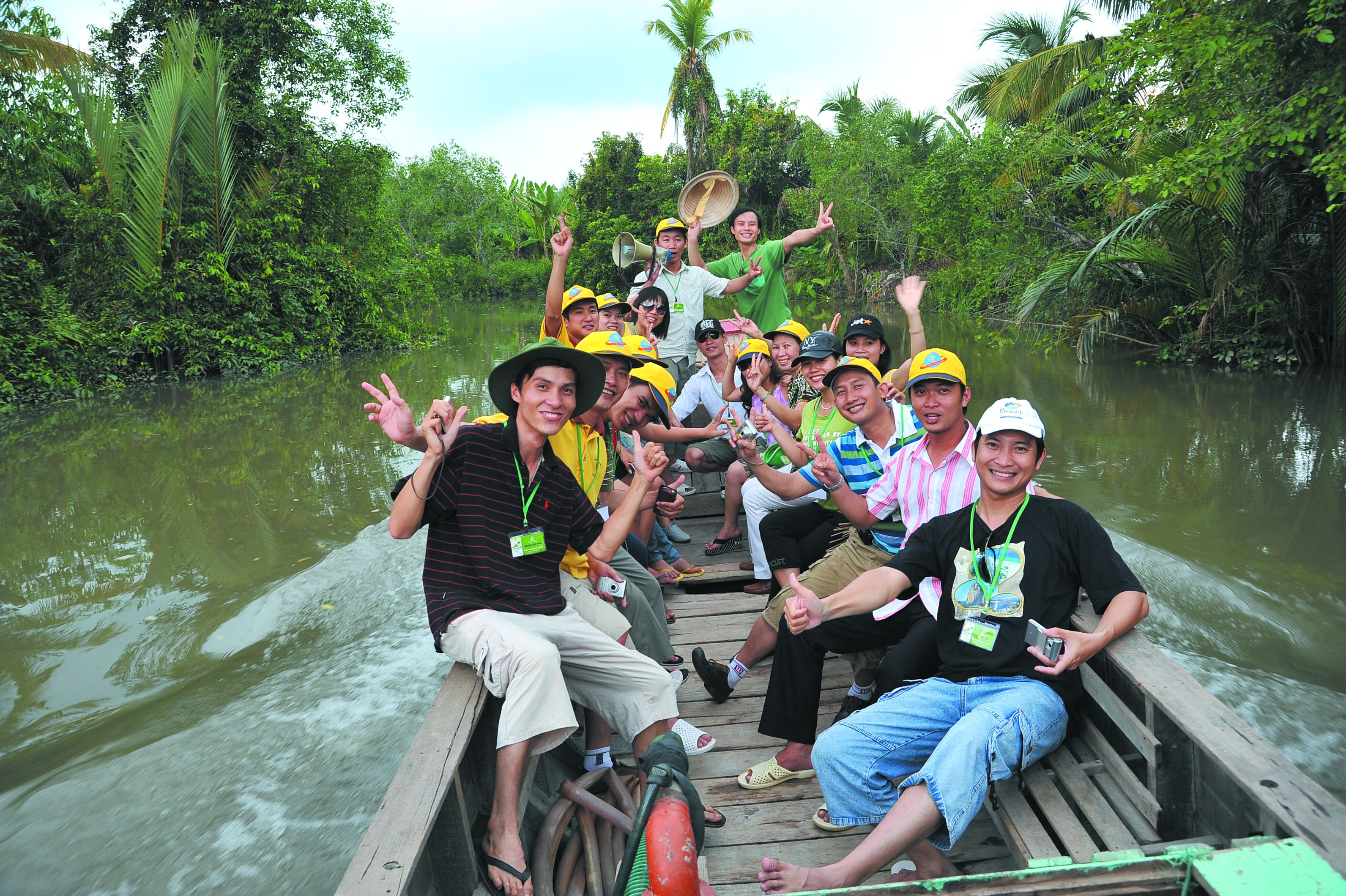 A group of people on a wooden boat in a river surrounded by dense greenery.