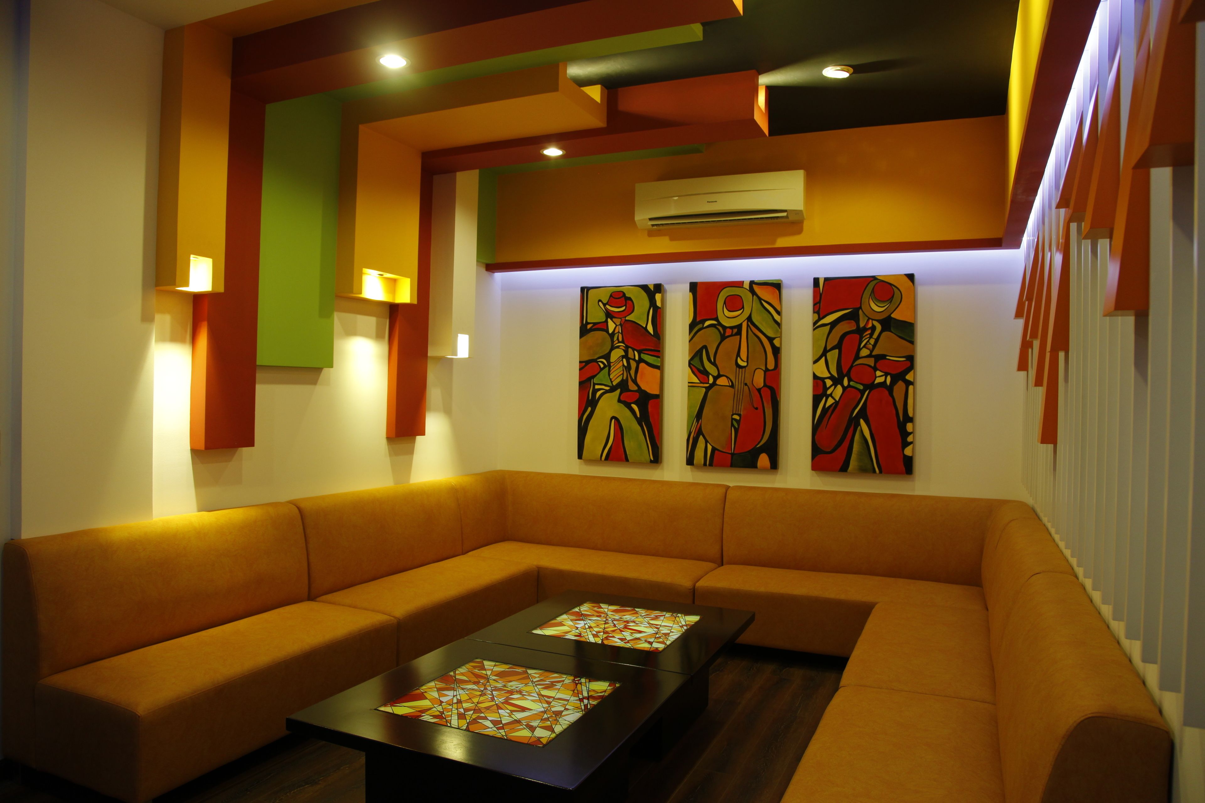 A modern living room with a sectional sofa, two coffee tables with geometric patterns, and three abstract paintings on the wall.