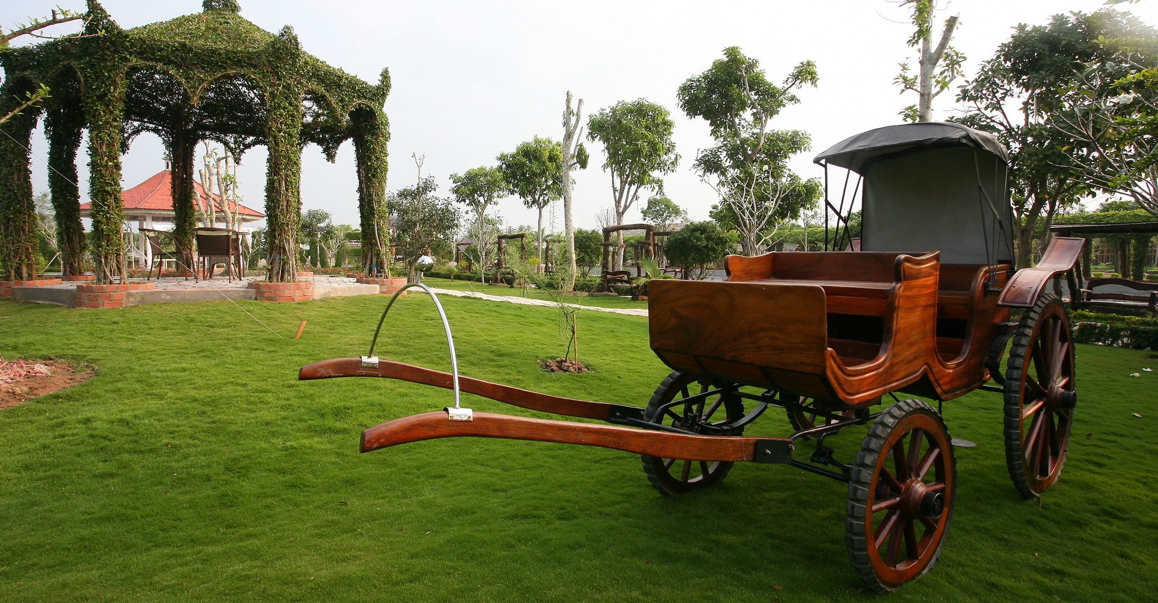 A wooden carriage with a canopy, parked on a well-manicured lawn.