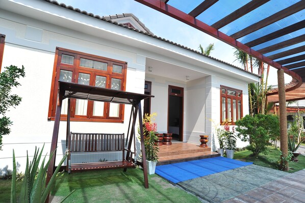 A two-story house with a covered porch, a wooden swing, and a small garden with potted plants. - Forever Green Resort (Phu Tuc)