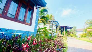Une maison à l’extérieur bleu et blanc, avec un toit en tuiles et un jardin où poussent différentes plantes et fleurs.