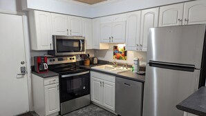 A compact kitchen with white cabinets, a stainless steel refrigerator, a microwave, an oven, a dishwasher, and a coffee maker. - "Couples & Family Getaway" – First Floor Villa, Pool & Beach Access (Hilton Head Island)