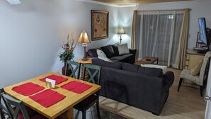 A cozy living room with a wooden ceiling, a dining table with red placemats, a sofa with cushions, and a TV on a wooden cabinet. - "Couples & Family Getaway," 1st Floor, King & Queen Beds, Pool, 42" HDTV's, WIFI (Hilton Head Island)