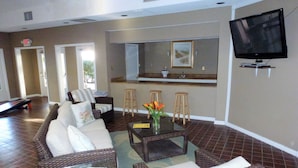 A living room with a sofa, a coffee table, and a television. There is a kitchen area with a counter and stools. - "Couples & Family Getaway," 1st Floor, King & Queen Beds, Pool, 42" HDTV's, WIFI (Hilton Head Island)