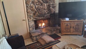 A stone fireplace with a fire, a television on a wooden cabinet, and a sofa with cushions.