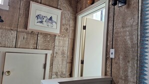 A rustic bathroom with wooden walls, a framed horse painting, a white door, and a mirror.