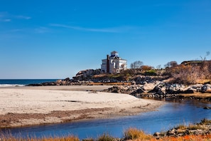 A coastal house with a prominent tower, situated on a rocky shoreline with a beach and a small stream. - Good Harbor Beach House - walk to beach, close to restaurants and shopping! (Gloucester)