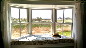 A bay window with a view of a grassy field and distant buildings.
