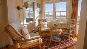 A cozy living room with a large window, a wicker side table, and a patterned rug.