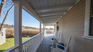 A covered porch with white railings, wooden flooring, and rocking chairs.