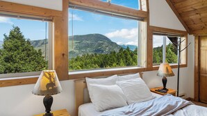 A bedroom with a bed, two nightstands, lamps, and large windows offering a mountain view. - Yellowstone Mountain Home-Secluded custom home near Yellowstone with privacy! (Emigrant)