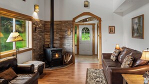 A cozy living room with a stone fireplace, leather sofas, and a view of the outdoors. - Yellowstone Mountain Home-Secluded custom home near Yellowstone with privacy! (Emigrant)