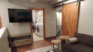 Una sala de estar con televisor de pantalla plana, un sofá, una mesa de centro con velas y una puerta de madera.