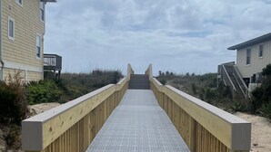 A wooden boardwalk leading to a beach with a building on one side. - Panoramic Ocean & Sound Views, 2 min walk to beach, Sleeps 8-10, Emerald Isle (Emerald Isle)