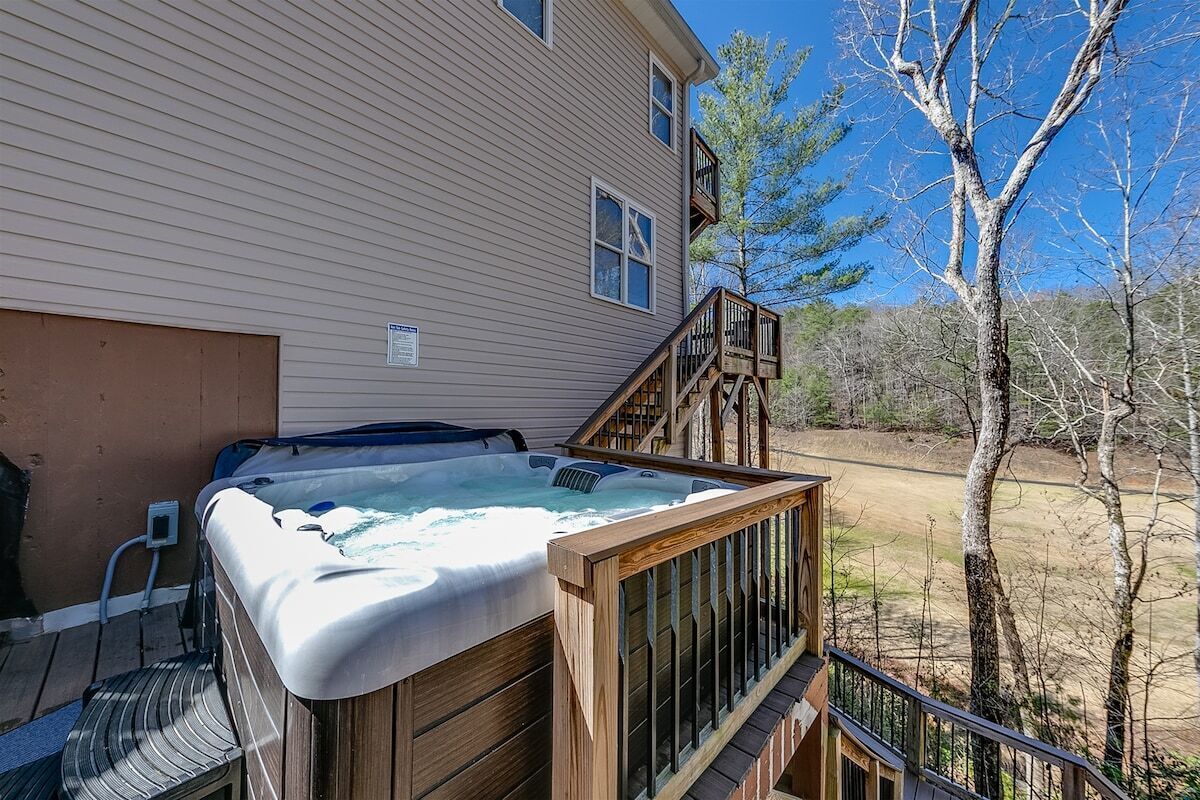 A hot tub on a wooden deck with a view of a house and trees.