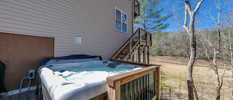 A hot tub on a wooden deck with a view of a house and trees.