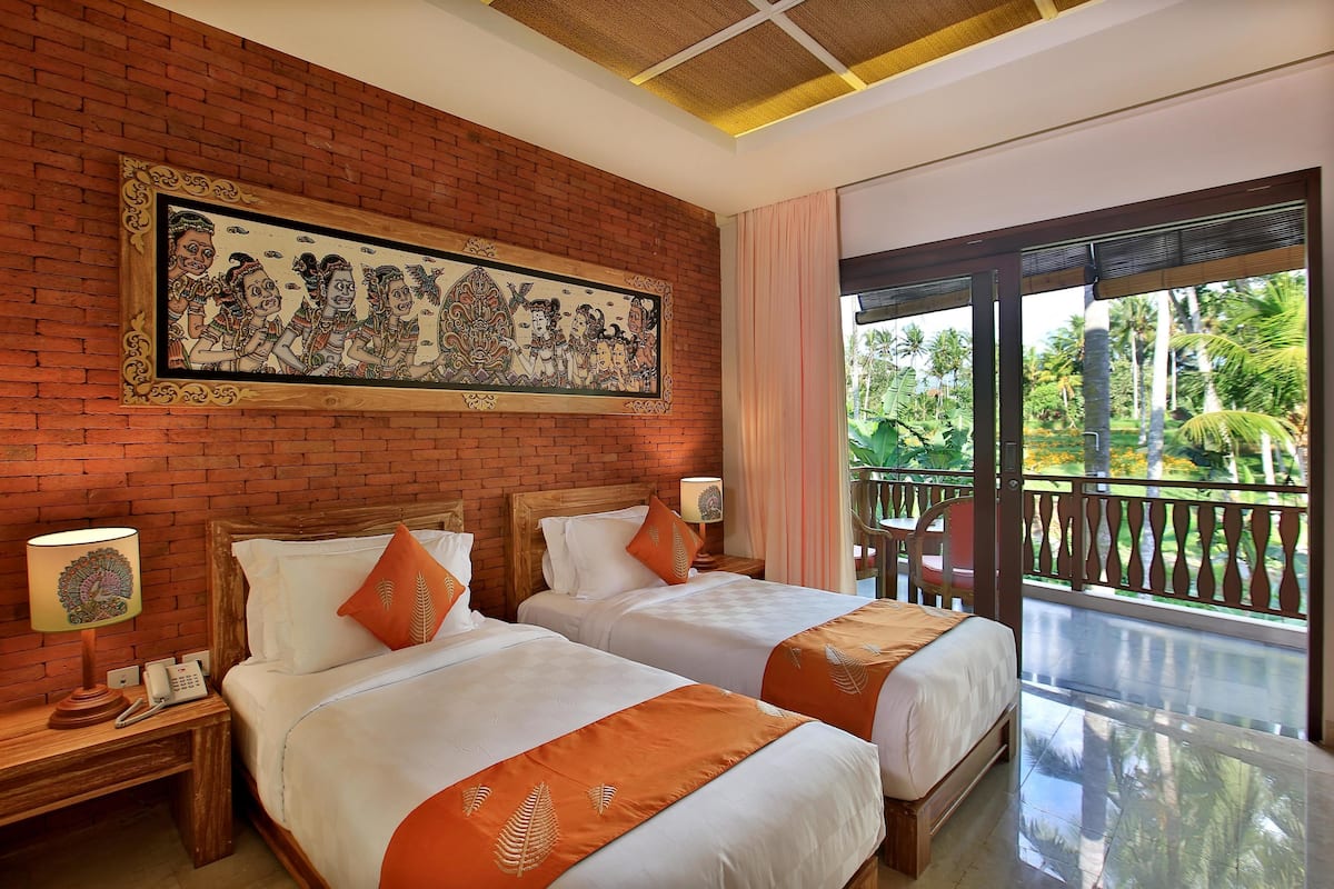 A hotel room with two beds, a large mural on the wall, a balcony with a view of palm trees, and a wooden headboard.